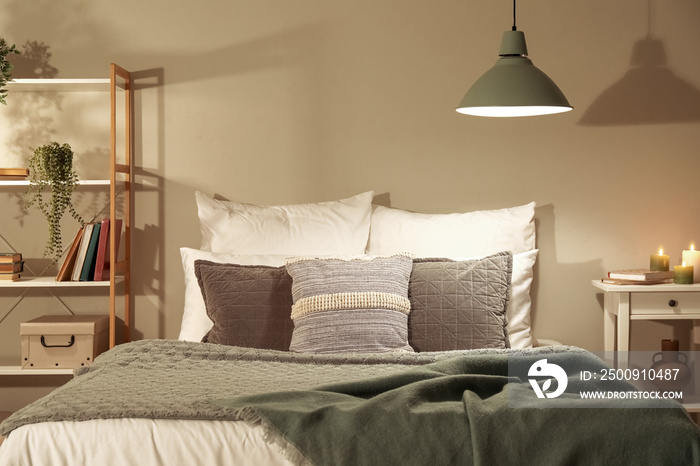 Interior of bedroom with green blankets on bed, burning candles and glowing lamps late in evening