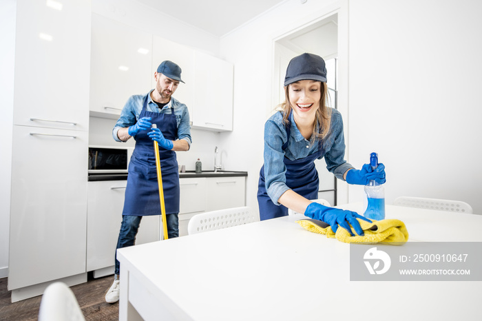 Man and woman as a professional cleaners in uniform washing floor and wiping furniture in the white 