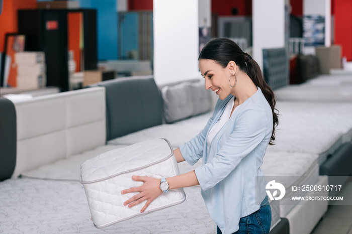 smiling woman with folding mattress in hands in furniture shop