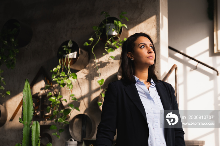 Arabic young elegant woman standing and looking out the window, illuminated by natural lighting. Fem