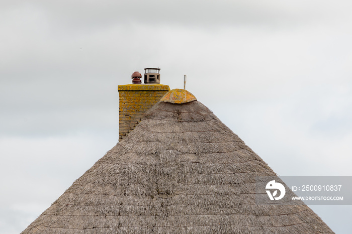 Traditional countryside houses with reed roof with chimney under white grey cloudy sky in raining da