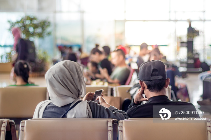 Modern muslim islamic asian couple using their smartphone apps while sitting and waiting for flight 