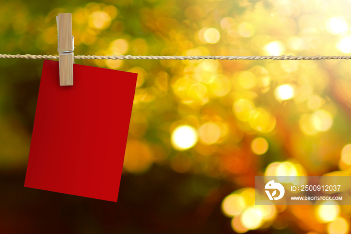 Blank sheets of red paper hang on a rope with clothespin on bokeh background.