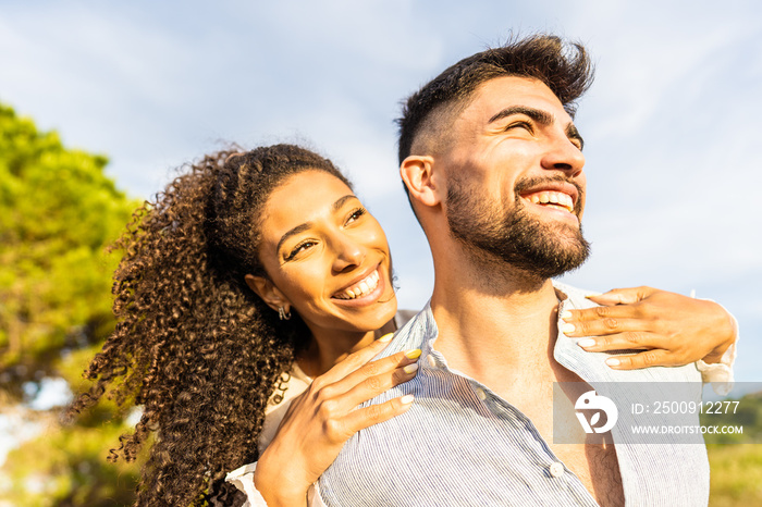 Multiracial happy young beautiful couple in love having fun outdoor in nature at dusk looking at hor