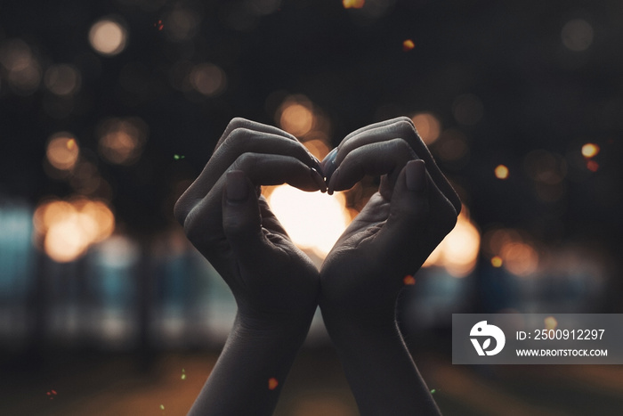 Romantic scenery, female hands folded into a heart shape on a blurred background of evening lights w