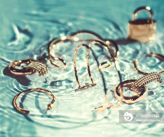 Golden bracelets, earrings, rings, jewelery on emerald water background, luxury glamour and holiday 