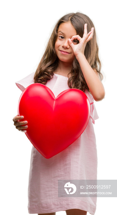 Brunette hispanic girl holding red heart with happy face smiling doing ok sign with hand on eye look