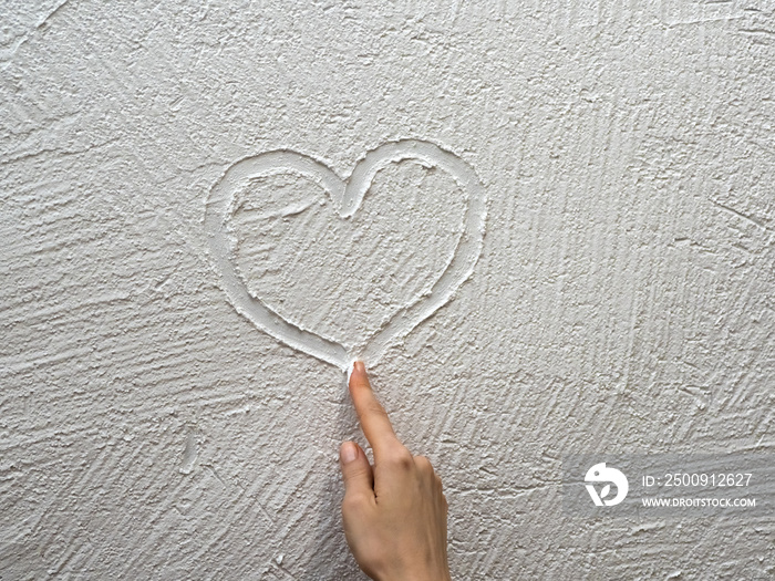 finger paints a heart on a white stucco wall.