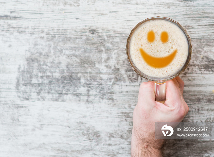 mans hand holds a mug of beer with smile on the foam . Space for text