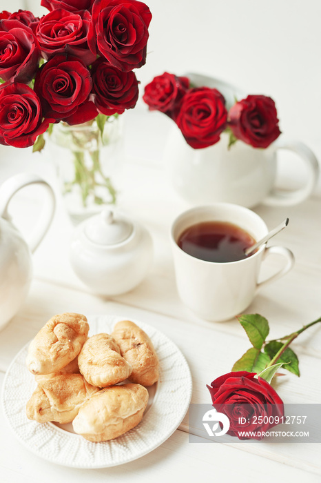 red roses, tea and croissants on a table near the window, romantic breakfast for Valentines Day