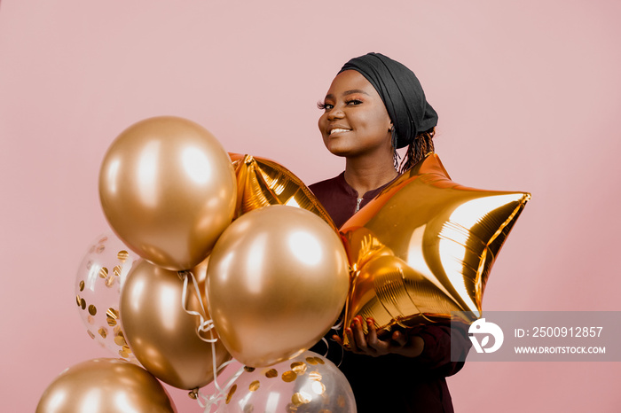 Black girl with golden ballons have a party and smile isolated on pink background. African woman cel