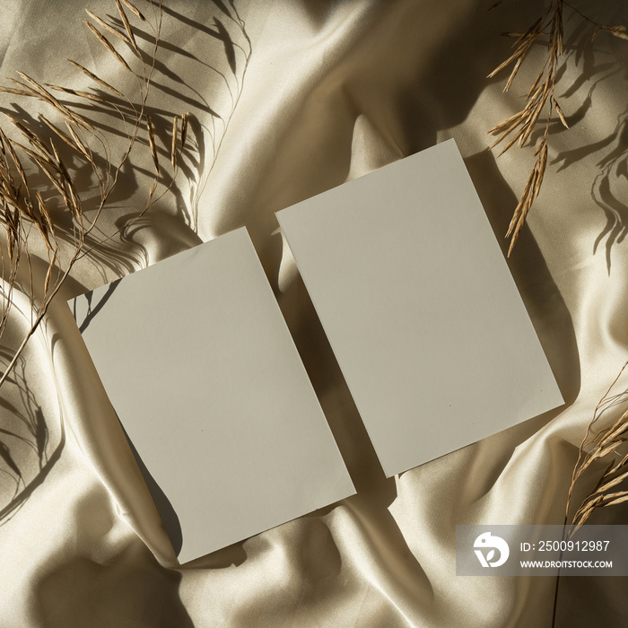 Paper cards sheet with blank mockup copy space and dried grass on glossy gold silk cloth background.