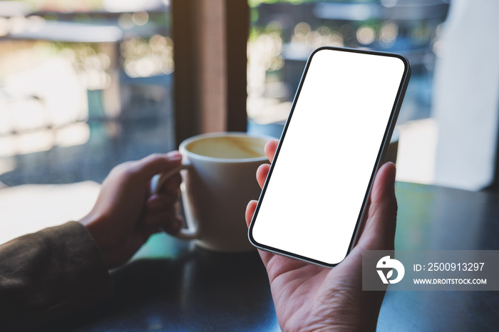 Mockup image of hands holding mobile phone with blank desktop screen while drinking coffee