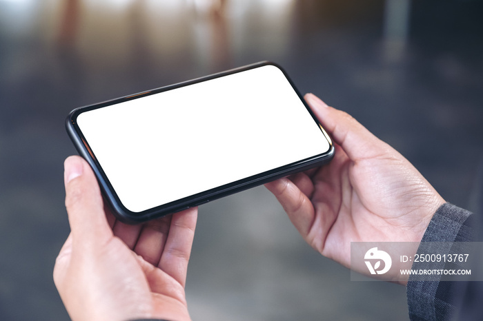 Mockup image of hands holding black mobile phone with blank white screen  horizontally