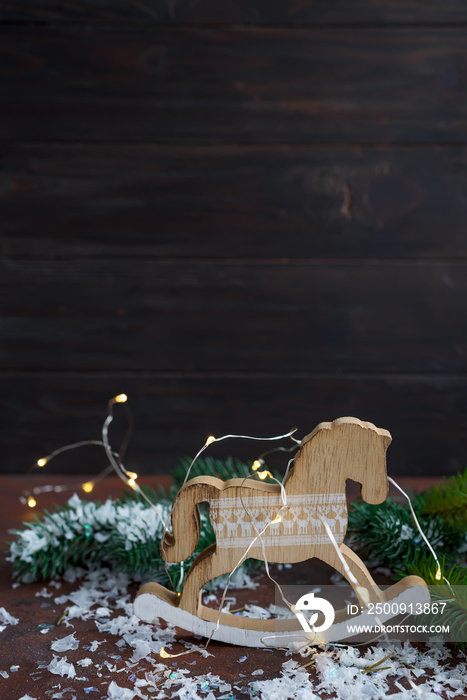 Toy wooden rocking horse as of New Years decorations with snow and fer tree on a wooden background