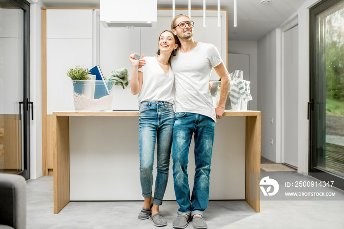 Young and happy couple enjoying their new modern apartment standing at the kitchen with different ho