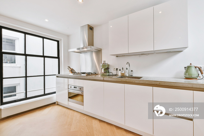 Interior of spacious kitchen with white cabinets and stainless extractor hood and black counter