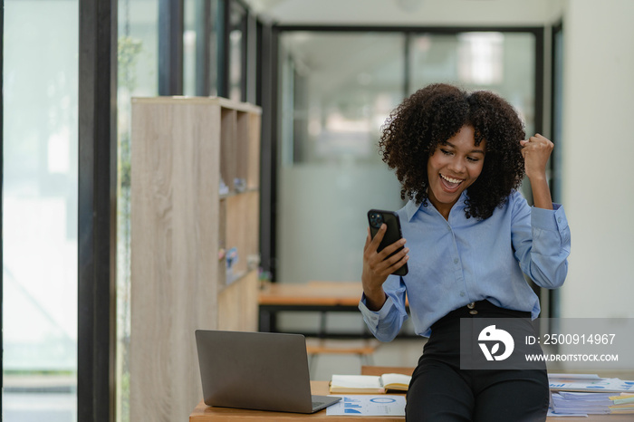 African-American businesswoman working on laptop at office using smartphone and financial graphs, ac