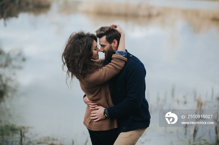 two caucasian lovers near the lake. Young couple is hugging on autumn day outdoors. A bearded man an