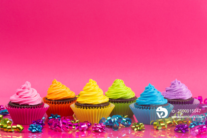 Rainbow Colored Frosted Chocolate Cupcakes on a Bright Pink Background