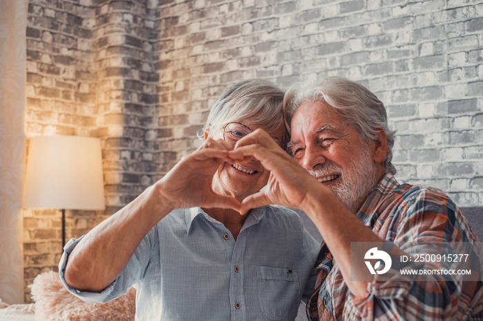 Close up of hands of two mature grandparents making a heart shape with their fingers together. Smili