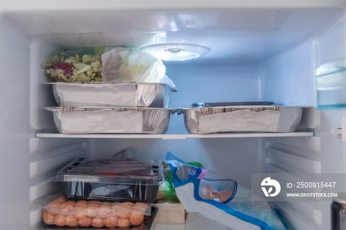 Open refrigerator filled with raw food, vegetables and foil package