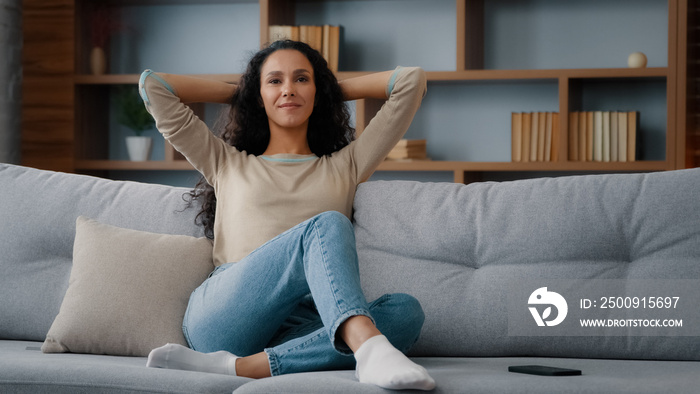 Calm happy in good mood caucasian hispanic latino 30s woman resting on couch new sofa in living room