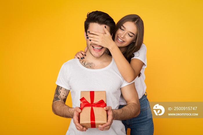 Girl covering boyfriend eyes and giving him present