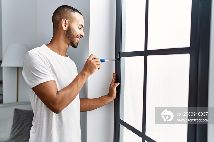 Young hispanic man smiling confident reparing window at home