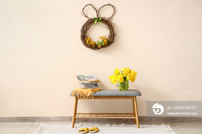 Bench with magazines and beautiful tulips near color wall with Easter wreath in room