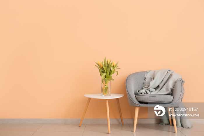 Interior of modern room with comfortable armchair and table with spring flowers near color wall