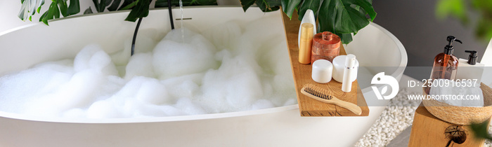 Modern bathroom interior with white bubble filled bathtub and monstera tropical plant. Eco body care