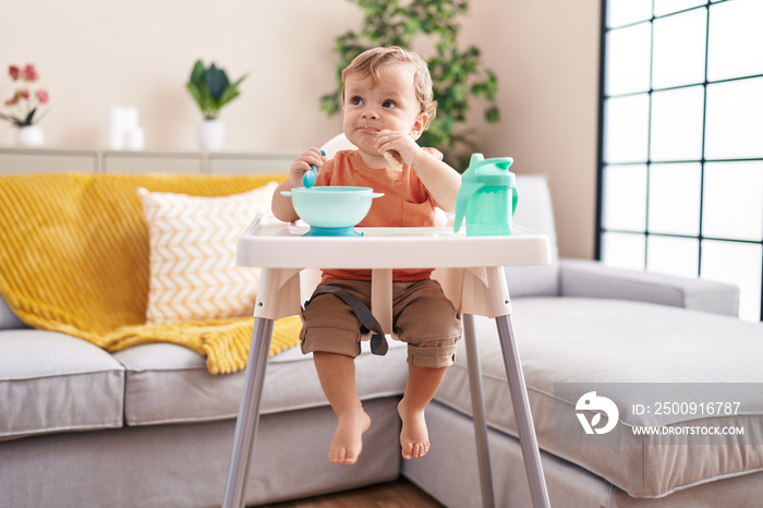 Adorable blond toddler sitting on highchair eating snack at home