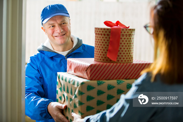 Delivery man bringing holiday packages. Woman at home standing in doorway, receiving parcels for Chr