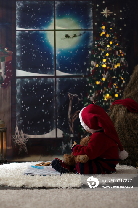 Sweet toddler boy, reading book at home at night on Christmas