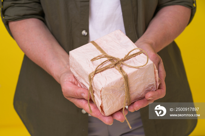 Mature woman with gift box in hands isolated on yellow background. Senior woman with a gif wrapped i