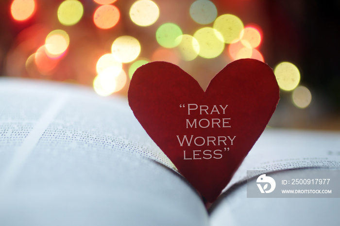 Inspirational quote on a red heart - Pray more, worry less. Spiritual text message on an open bible 