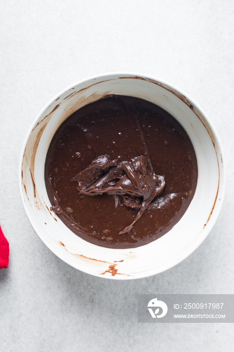 Thick chocolate madeleine batter that has rested in a white bowl, thick chocolate cake batter