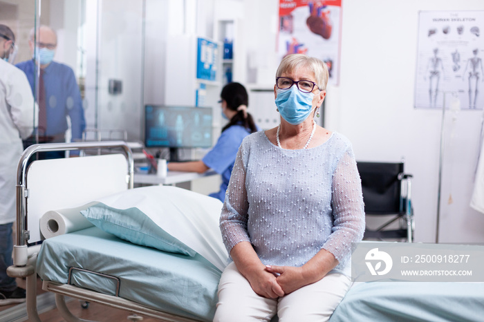 Elderly woman wearing face mask against covid while waiting for doctor in hospital cabinet for medic