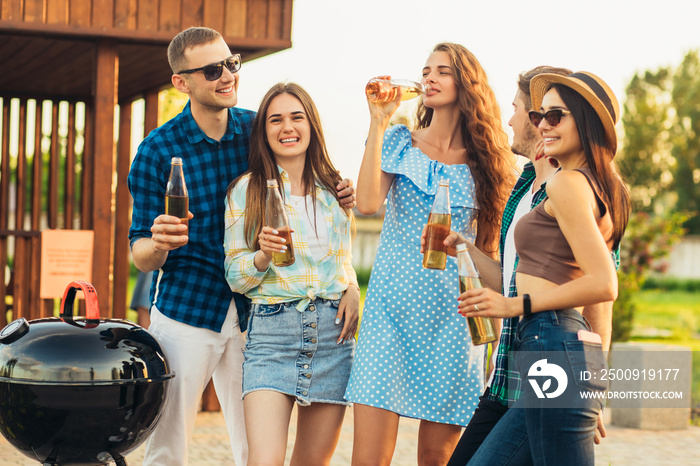 Group of young friends having barbecue party in nature, friends fry meat, chat and drink lemonade ou