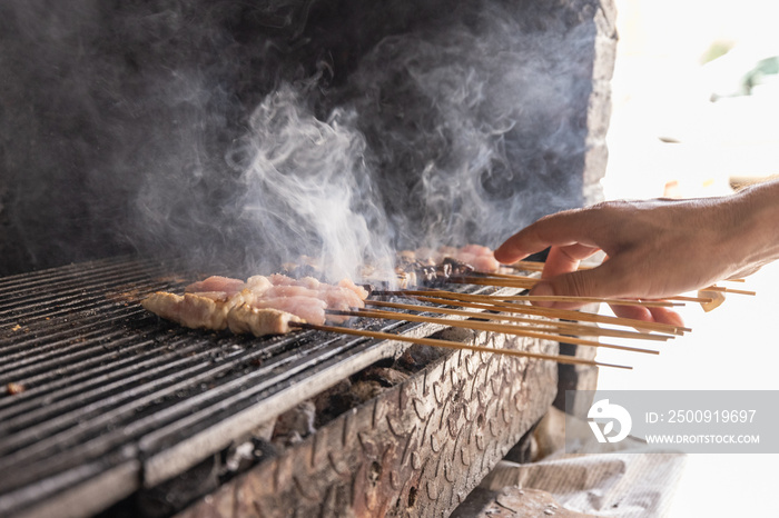 Flipping around meat on wooden sticks, algerian traditional food, over a hot charcoal grill. Smoke r