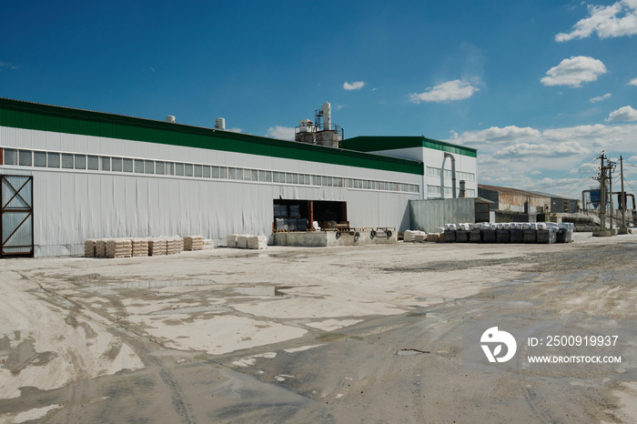 Part of long building of modern industrial factory of white color standing along wide asphalted yard