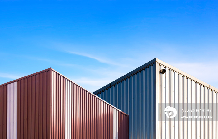 Low angle view of 2 modern brown and silver corrugated steel industrial building against blue sky ba