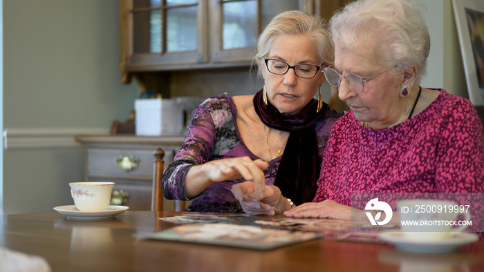 Senior elderly smiling woman looking at old photos and remembering memories with daughter at the din