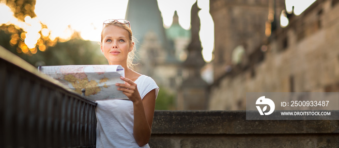 Pretty young female tourist studying a map, enjoying discovering a new city, looking excited (shallow DOF; color toned image)