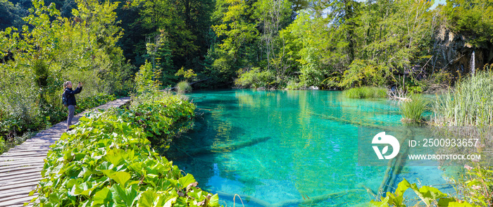 Female hiker taking photo of the stunning turquoise lake and trees of Plitvice National Park