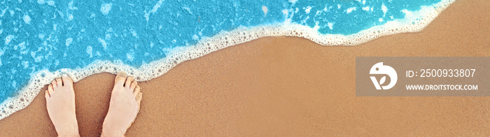 Soft blue ocean wave on clean sandy beach with human feet, top view