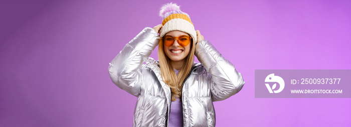 Energized daring sassy young attractive woman having fun friends winter trip learn snowboarding smiling cheeky enjoying vacation put-on hat wearing silver warm jacket sunglasses, purple background