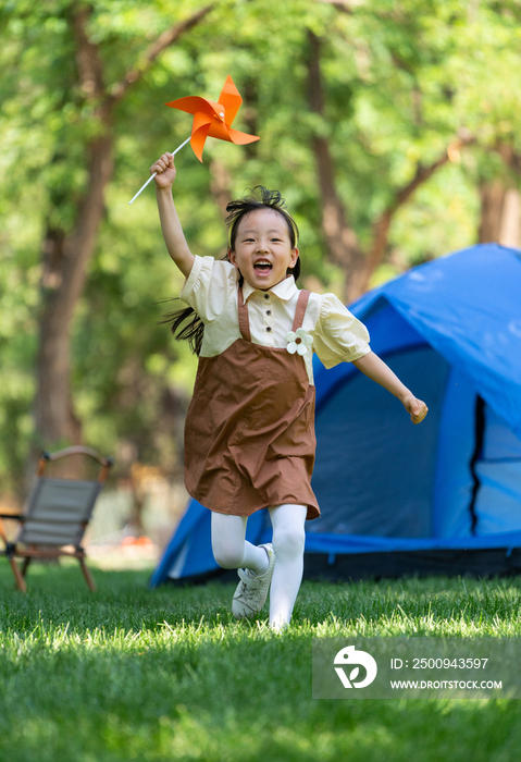 小女孩在草地上举着风车开心奔跑