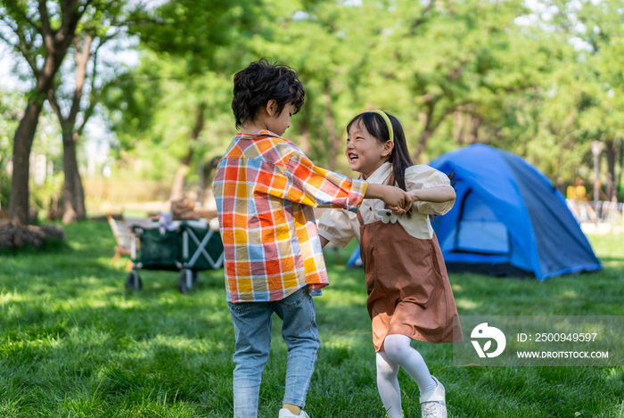 两个孩子在草地上手拉手开心转圈做游戏